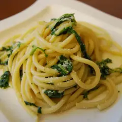 Pyszny makaron bucatini z zielonymi liśćmi i startym parmezanem na białym talerzu.