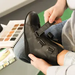 Mann passt orthopädische Schuhe an. Materialmuster und Schuhkatalog liegen bereit. Die orthopädische schuhe kosten sind hier ein wichtiges Thema.