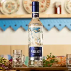 Butelka wódki Finlandia z kieliszkami i przekąskami na stole.
