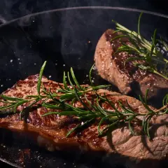 Zwei saftige Rumpsteaks braten in einer Pfanne, garniert mit Rosmarin und grobem Salz. Dampf steigt auf und verheißt ein köstliches Mahl.