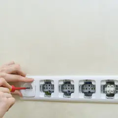 Montaż gniazdek elektrycznych. Ręce przykręcają śrubokrętem jedno z gniazdek w listwie. Schemat instalacji elektrycznej.