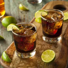 Dwa drinki z rumem i colą, ozdobione ćwiartkami limonki, leżą na drewnianej desce. Idealne z czym pić rum!