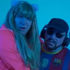 Dos personas con peluca y gorra, una con camiseta del Barça, parecen estar cantando la letra de "el pantalon".