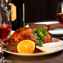 Idealne jakie wino do gęsi? Czerwone wino i pieczona gęś z pomarańczą i ziołami, na elegancko zastawionym stole.