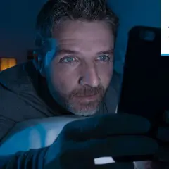 Mężczyzna wpatruje się w ekran telefonu w ciemności, jego oczy błyszczą. Czy to uzależnienie od muzyki, czy od mediów społecznościowych?
