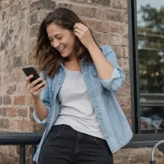 Uśmiechnięta dziewczyna z telefonem w ręku, zastanawia się, co napisać dziewczynie.