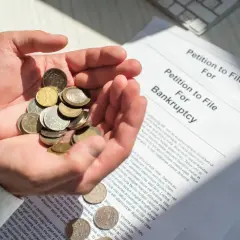 Dłonie trzymają garść monet obok dokumentu "Petition to File For Bankruptcy". To obrazuje, co się dzieje po ogłoszeniu upadłości konsumenckiej.