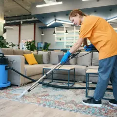 Mujer con guantes azules usa una aspiradora para limpiar alfombras con fregona en una sala de estar moderna.