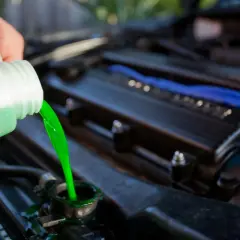 Vertiendo líquido refrigerante verde brillante en el radiador de un coche. El nivel líquido refrigerante es crucial para el motor.