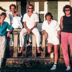 Członkowie Dire Straits pozują na tle budynku. Jeden z nich trzyma gitarę.