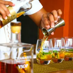Barman nalewa alkohol do szklanek, przygotowując drinki. Widać butelki i kieliszki z lodem i miętą. Odkryj nowe smaki wódki!