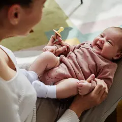 Mama bawi się z dzieckiem, które radośnie gaworzy, trzymając smoczek.