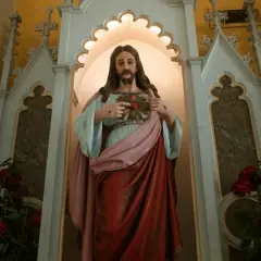 Figurka Jezusa z Sercem, wskazująca na nie, mówi "jestem który jestem". Czerwone róże u stóp.