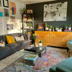 Salon w stylu maksymalistycznym: szara sofa, turkusowe fotele, kolorowy dywan, mnóstwo roślin i dekoracji na ścianach.