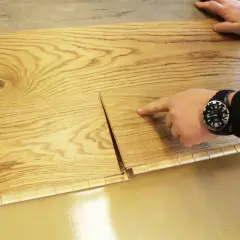 Hände zeigen, wie man Parkett selbst verlegt. Holzmaserung und Klickverbindung sind gut sichtbar.