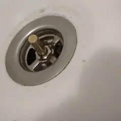 Korek do wanny z pokrętłem, widoczny mechanizm do naprawy. Widać włosy i brud wokół odpływu.