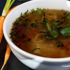 Aromaticzny rosół kolagenowy z marchewką i natką pietruszki, obok świeże marchewki.