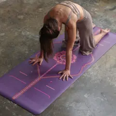 Mujer en postura de la esfinge sobre una esterilla de yoga morada con diseño.