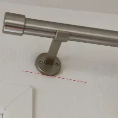 Eine silberne Gardinenstange wird an der Wand befestigt. Die Halterung ist mit Schrauben gesichert.