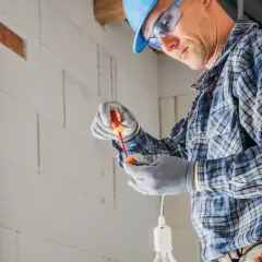Elektryk w kasku i okularach montuje oprawkę żarówki. Zastanawia się, ile za punkt elektryczny.