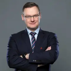 Miłosz Stępiński w granatowym garniturze, z rękami skrzyżowanymi na piersi, patrzy pewnie w obiektyw.