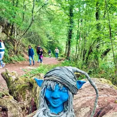 Un duende azul vigila las rutas con niños en Asturias. Familias disfrutan del sendero boscoso.