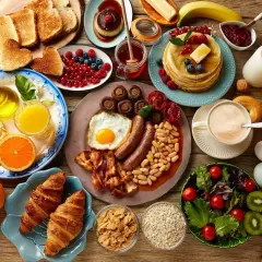 Un copieux repas sportif : œufs, saucisses, haricots, toasts, fruits, pancakes, croissants, café et jus d'orange.
