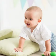 Uśmiechnięte dziecko w białej koszuli i pasiastych spodenkach próbuje wspiąć się na poduszkę, niedługo kiedy dziecko siada.