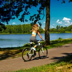 Kobieta na rowerze podziwia malownicze **trasy rowerowe Mazury**. Słońce, jezioro i las tworzą idealne tło.