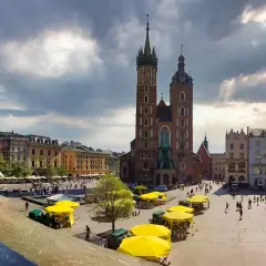 Małe dziecko w czapce z daszkiem patrzy na Rynek Główny w Krakowie. W tle Bazylika Mariacka i kolorowe kamienice.