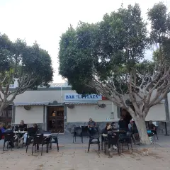 Gente disfrutando en la terraza de "Bar La Plaza", uno de los mejores restaurantes de Cabo de Gata, bajo la sombra de árboles frondosos.