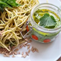 Makaron z domowym pesto z pokrzywy, ozdobiony świeżymi liśćmi i pestkami słonecznika. Pesto w słoiczku wygląda apetycznie.