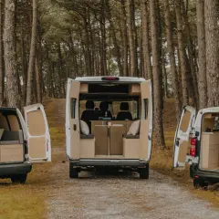 Trois camping-cars aménagés, dont un dimension camping-car 4 places, garés dans une forêt.