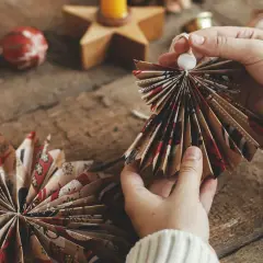 Ręce składają papierowy aniołek. Widać jak zrobić aniołka z ozdobnego papieru, tworząc skrzydła.