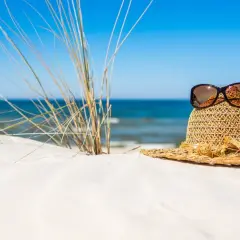 Słomkowy kapelusz z okularami przeciwsłonecznymi na piaszczystej plaży, idealny na wyjazd gdzie nad morze.