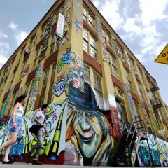 Gelbes Gebäude mit Graffiti-Kunst, Menschen gehen vorbei, "DEAD END"-Schild.