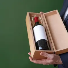 Elegancki mężczyzna w garniturze prezentuje drewniane pudełko z butelką wina wytrawnego czerwonego.