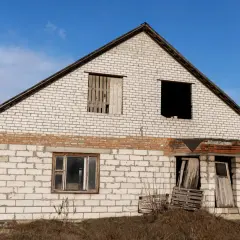 Dom w budowie, grożący zawaleniem, czeka na rozbiórkę. Okna zabite deskami, drzwi rozbite.