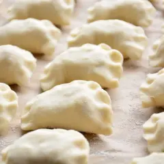 Gotowe do gotowania ciasto na pierogi, ułożone rzędami na blacie.