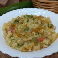 Un piatto invitante di pasta e zucchine alla pugliese, con fagioli e pomodoro, condito con erbe aromatiche.