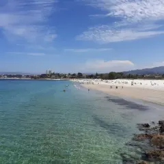 Amplia vista de la playa del Vao en Vigo, con aguas cristalinas, arena blanca y gente disfrutando del sol.