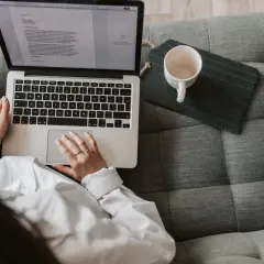 Scenarzysta pracuje nad nowym tekstem na laptopie, siedząc wygodnie na kanapie. Obok leży pusta filiżanka.