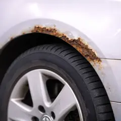 Rdza postępuje na nadkole srebrnego samochodu, niszcząc jego powłokę.