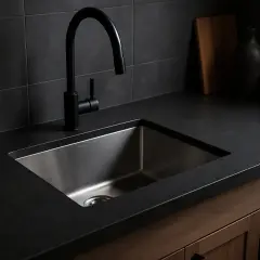 Nowoczesny zlew pod zabudowę ze stali nierdzewnej z czarną baterią, umieszczony na ciemnym blacie.