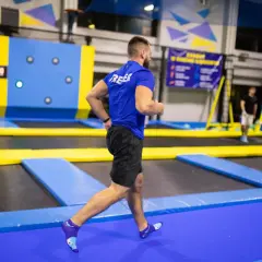 Mężczyzna w niebieskiej koszulce wykonuje trening interwałowy na trampolinach.