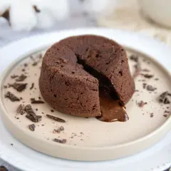 Ein warmes Schoko Soufflé mit flüssigem Kern, garniert mit Schokostückchen auf einem Teller.
