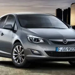 Srebrny Opel Astra J z nowoczesnymi światłami i felgami stoi na tle miejskiej panoramy.