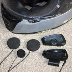 Akcesoria do interkomu motocyklowego Cardo i słuchawki JBL leżą obok kasku. Dowiedz się, jak zamontować interkom do kasku.