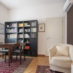 Arredamento accogliente per uno studio di psicoterapia: poltrona comoda, libreria piena e un tavolo per le sedute.