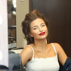 Julia Wieniawa z burzą loków i mocnym makijażem, w białej bluzce na ramiączkach.